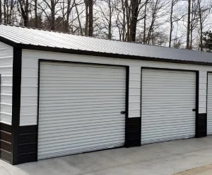 Two white garage doors on a black and white building surrounded by trees.