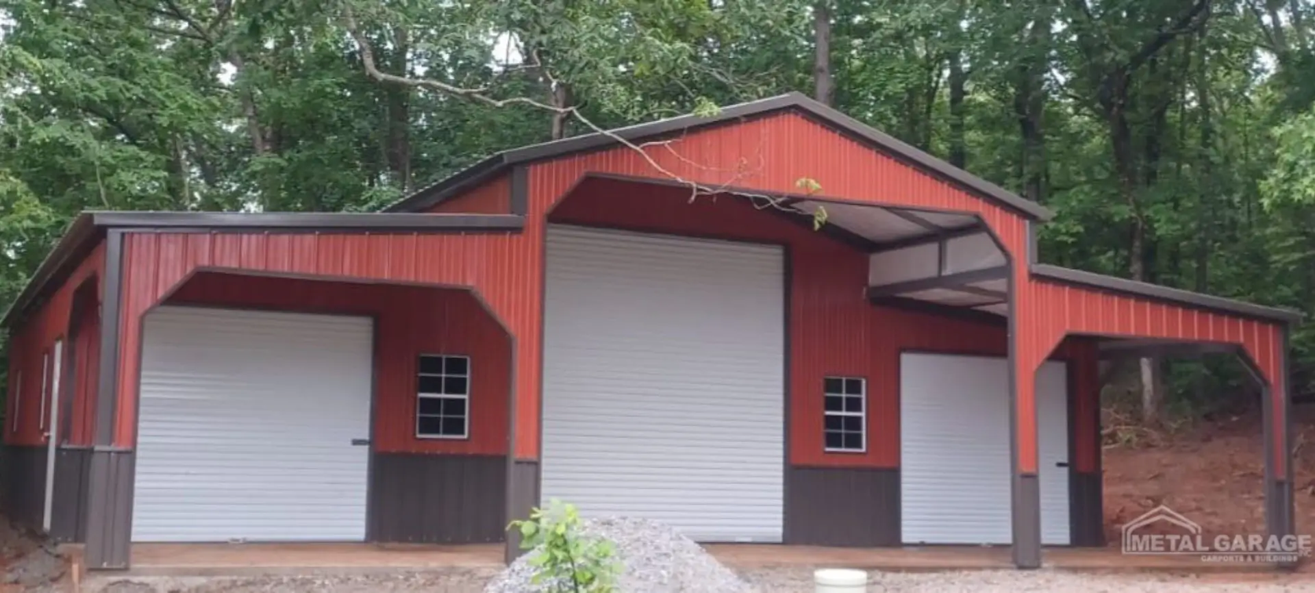 Red and black garage with a closed white roll-up door in a wooded area.